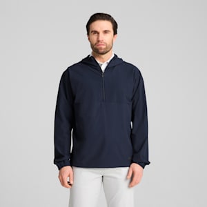 A model in front of a grey background wearing a navy jacket and light trousers.