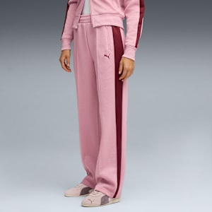 Against grey, a model wears pink trousers with a burgundy stripe and matching trainers.