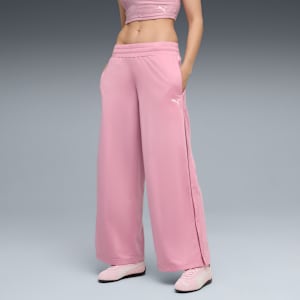 A model poses against grey wearing a pink top, wide-leg trousers with side fastenings, and trainers.