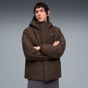 A model with crossed arms wears a brown patterned jacket against a grey backdrop.