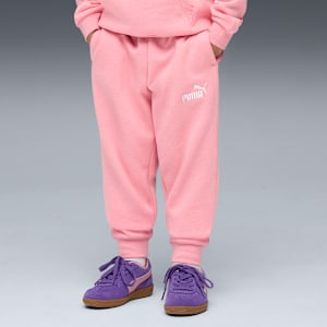 On grey, a model poses in pink sweats and purple trainers with tied laces.