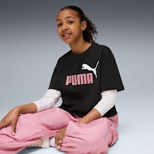 Model sits against grey background wearing a black Puma logo tee and pink trousers.
