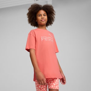 A model poses against a grey backdrop wearing a coral t-shirt and patterned shorts.