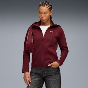 Model on grey background wears a maroon zip hoodie, jeans, and carries a shiny bag.