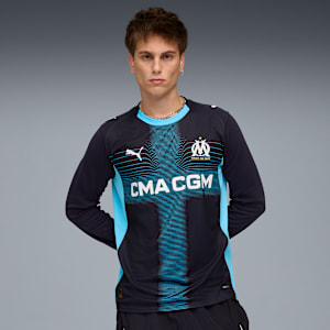 Against grey, a model poses wearing a long-sleeved black and blue sports shirt.