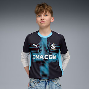 A model poses against a grey backdrop, wearing a patterned black and blue t-shirt and jeans.