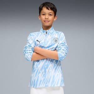 A model with crossed arms wears a light blue patterned top against a grey backdrop.