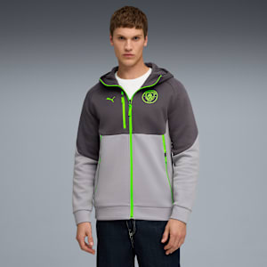 A model stands against a grey backdrop wearing a two-tone zip-up hoodie and dark jeans.