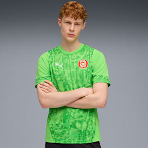 Against grey, a model with crossed arms wears a green patterned sports shirt.