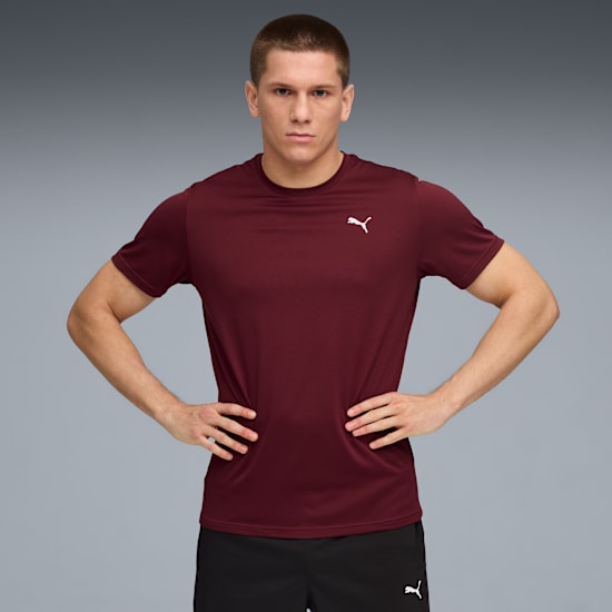 Su sfondo grigio, un modello posa con le mani sui fianchi, indossando una t-shirt bordeaux e pantaloncini neri.