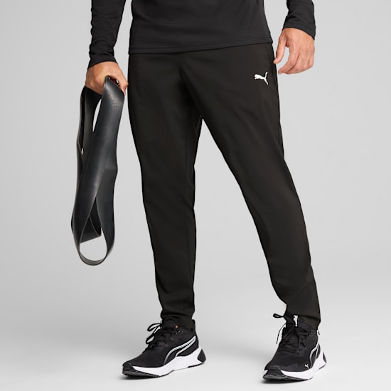 Against grey, a model holds a black resistance band wearing black activewear and trainers.