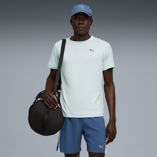 A model on grey wears a cap, t-shirt, shorts and carries a black duffel bag.