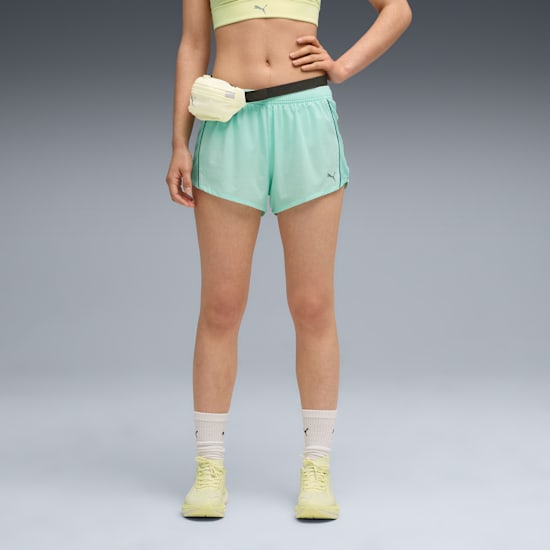 A model in a yellow top, mint shorts, socks and shoes stands against a grey backdrop.