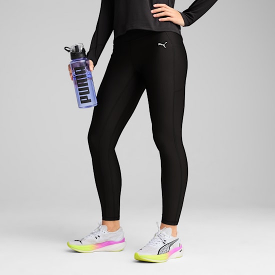 Against grey, a model poses in black activewear, holding a transparent water bottle.