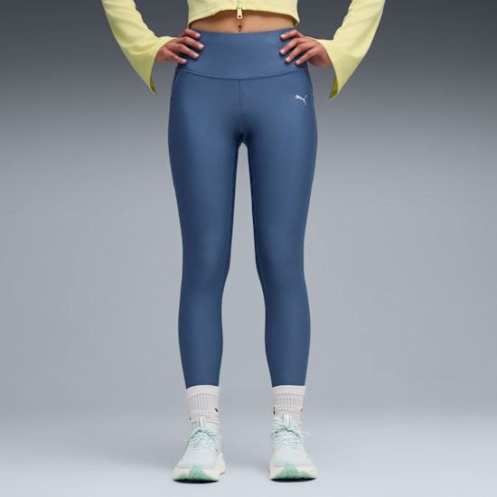 Un modèle se tient sur un fond gris, portant des leggings bleus, des baskets et des chaussettes.