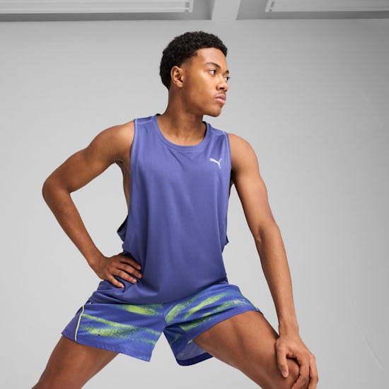 Tegen een grijze achtergrond rekt een model zich uit in een blauw shirt en een short met print.