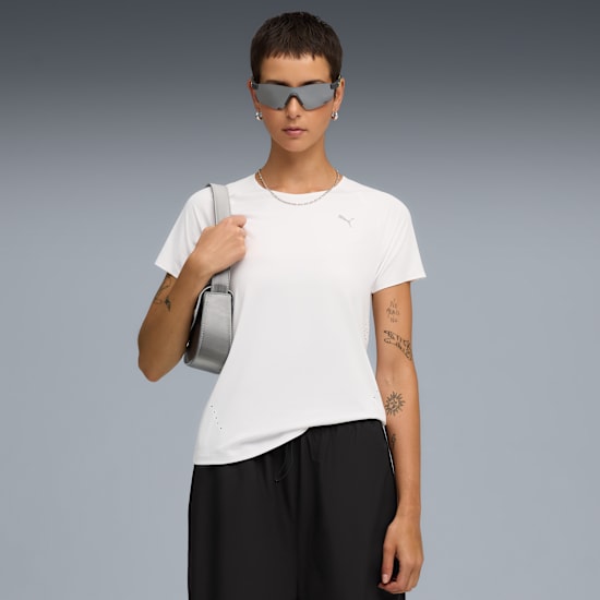 A model poses against a grey backdrop, wearing a white tee, black shorts and sunglasses.