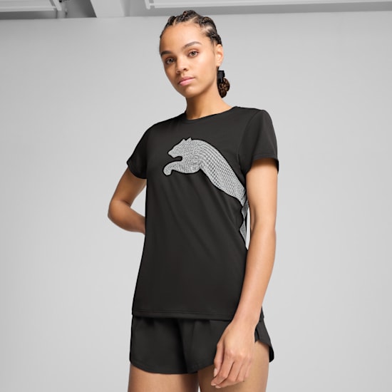 Against grey, a model poses in a black t-shirt with a light grey logo and black shorts.