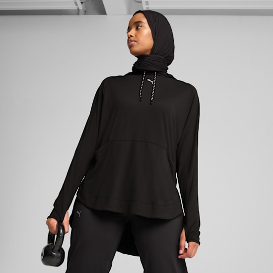 Tegen een grijze achtergrond houdt een model met een zwarte hijab en sportkleding een kettlebell vast.