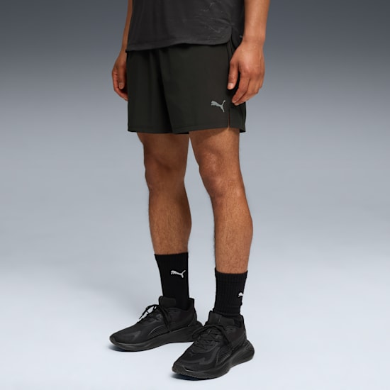 A model stands against grey wearing a t-shirt, shorts, socks and running shoes.
