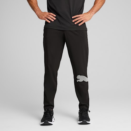 A model stands against grey, wearing a black t-shirt, trousers with logo, and trainers.