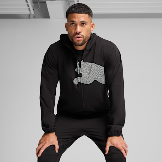 Un modèle se penche sur fond gris, portant veste à capuche noire et pantalon noir.