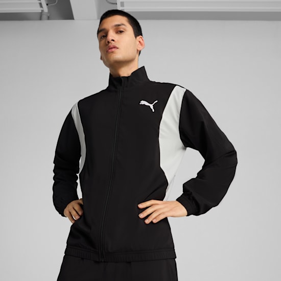 A model poses against grey wearing a black and white Puma jacket with hands on hips.