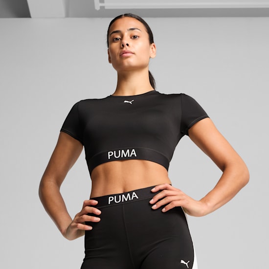 Tegen een grijze achtergrond poseert een model in een zwarte Puma crop top en legging.