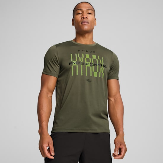 Un modèle pose sur fond gris, portant un t-shirt olive et un short noir.