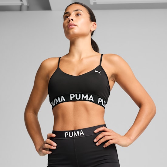 A model poses against grey in a black Puma sports bra and matching bottoms.