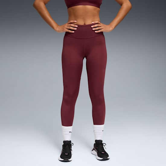 Against grey, a model poses in a maroon sports bra, leggings, white socks and black trainers.