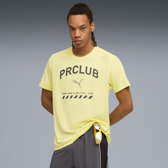 Against grey, a model wears a yellow 'PRCLUB' t-shirt and grey shorts, looking at the camera.