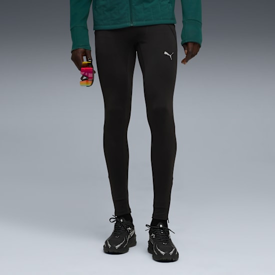 Against grey, a model wears running shoes, dark leggings, and a green jacket with a colourful bottle.
