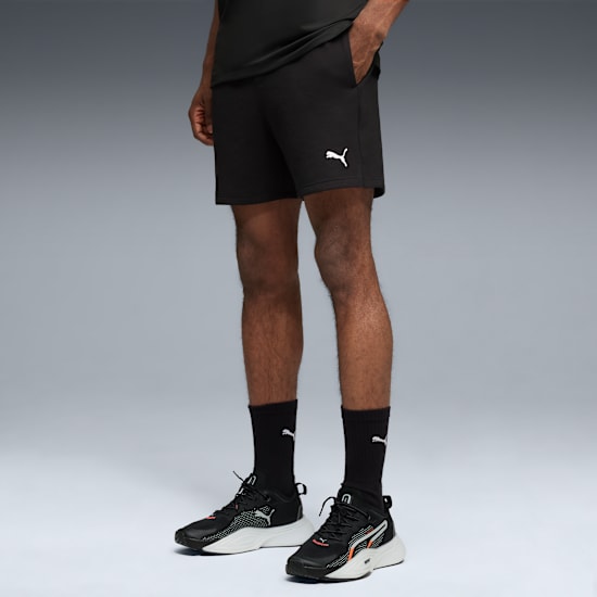 Un modello posa su sfondo grigio, indossando pantaloncini, calze e scarpe da ginnastica neri.