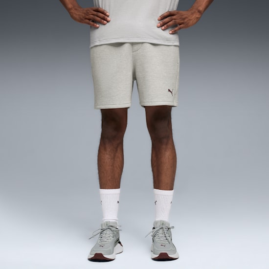 Against grey, a model poses in a light grey t-shirt, shorts, trainers and white socks.