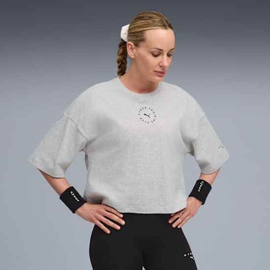 Against grey, a model in a grey t-shirt, black leggings and wristbands looks down.