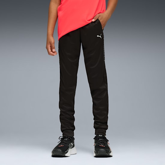 Na szarym tle model ma na sobie czerwoną bluzkę, czarne spodnie z logo i buty do biegania.