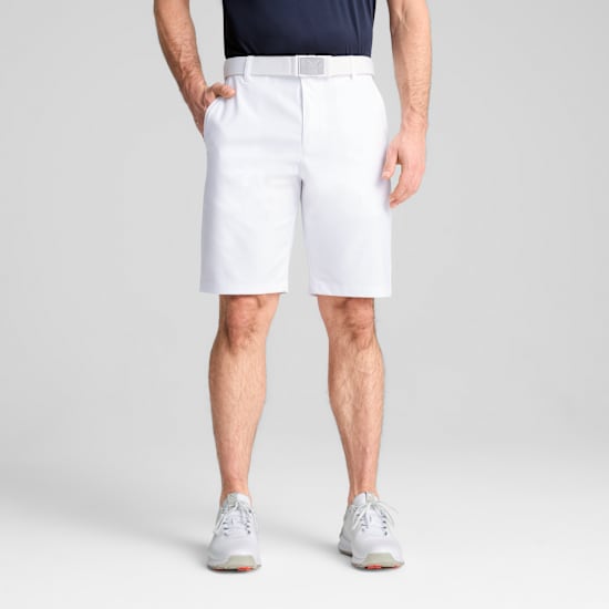 Ein Model posiert vor grauem Hintergrund mit weißen Shorts, Gürtel und Schuhen.