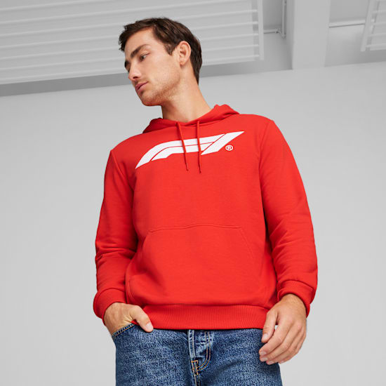Vor grauem Hintergrund blickt ein Model nach unten, es trägt einen roten Hoodie mit weißem Logo und Jeans.