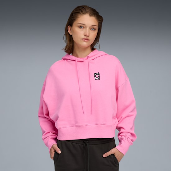 A model poses against grey, wearing a pink hoodie and dark-coloured trousers.