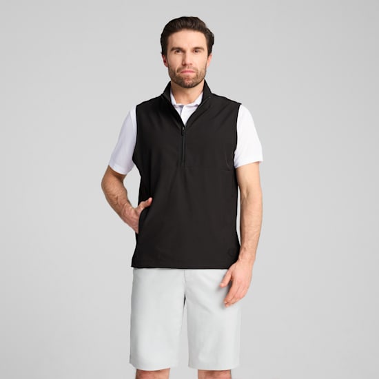 A model poses against a grey backdrop, wearing a white t-shirt, black vest and light shorts.