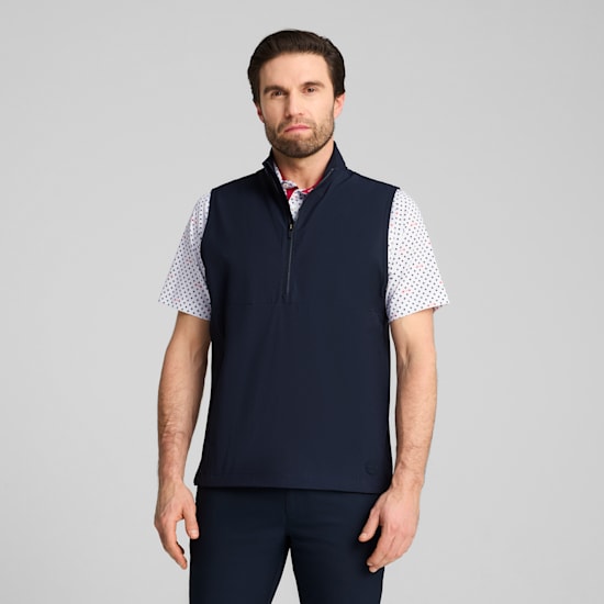 A model stands against a grey background wearing a navy vest, patterned shirt and trousers.