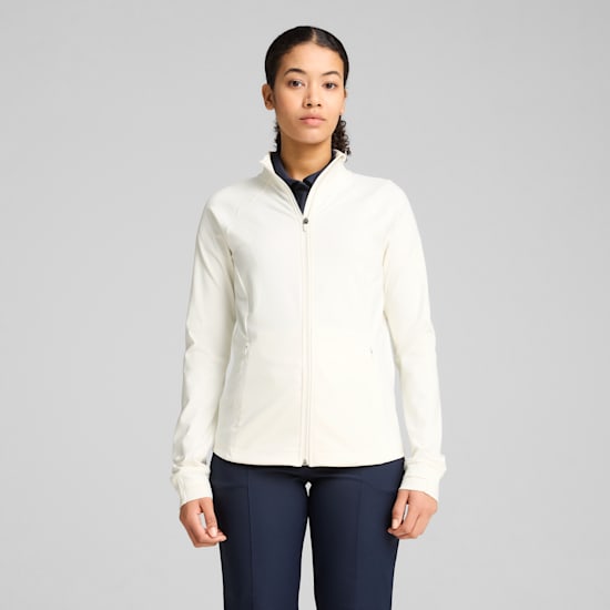 Against grey, a model stands wearing an off-white zip jacket and dark trousers.