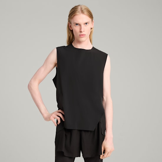 Ein Model posiert vor grauem Hintergrund mit schwarzem Top und Shorts.