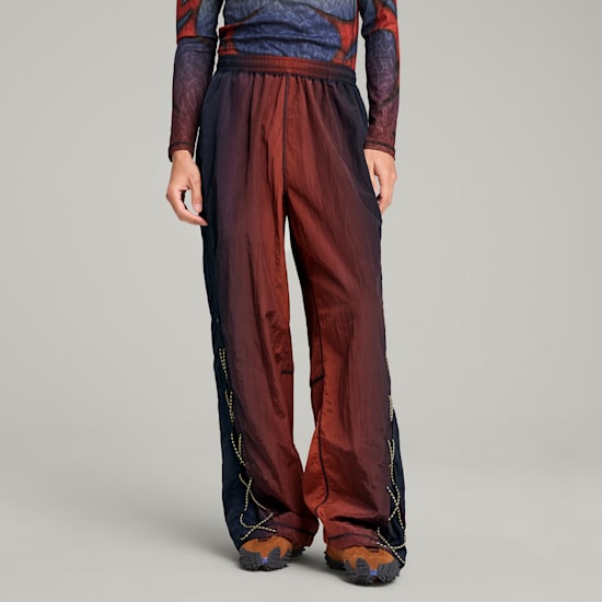 A model stands against a grey backdrop, wearing patterned top and gradient trousers with detailed shoes.