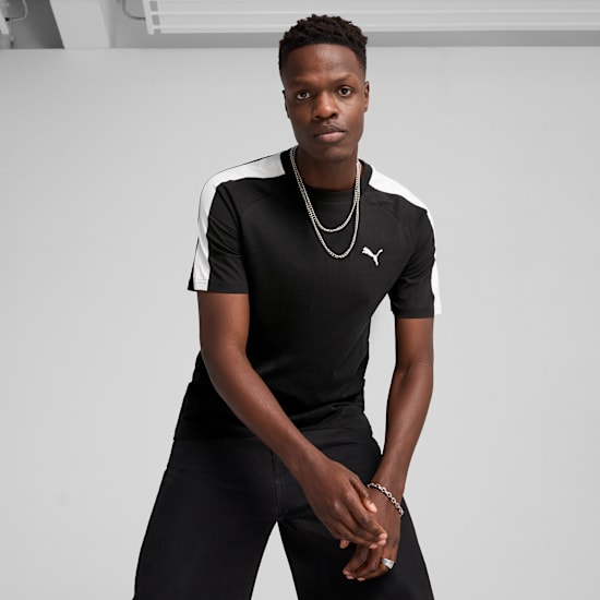 A model poses against a grey backdrop, wearing a black t-shirt and black trousers.