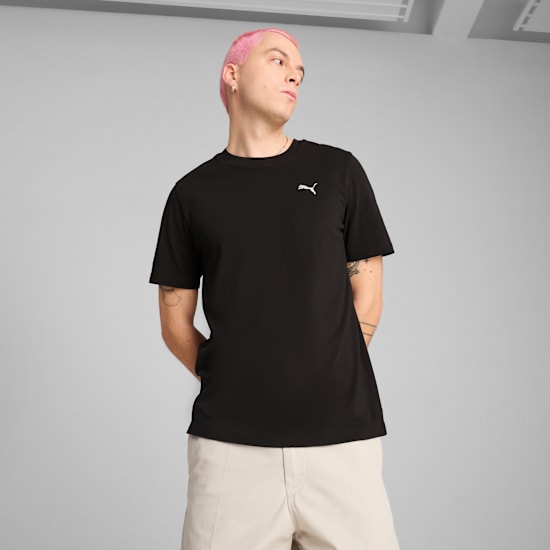 Een model met roze haar poseert voor een grijze achtergrond, gekleed in een zwart T-shirt.