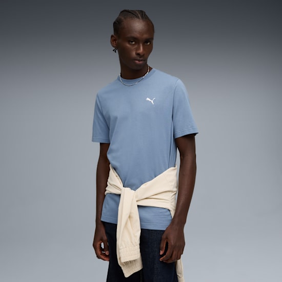 Un mannequin pose sur fond gris, portant un t-shirt bleu, un jean et un pull crème noué.