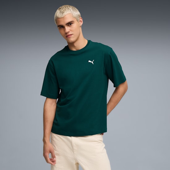 A model poses against grey wearing a dark green tee and light trousers.