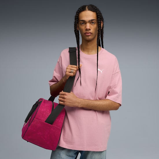 Ein Model mit Zöpfen posiert vor Grau mit rosa T-Shirt und rosa Seesack.